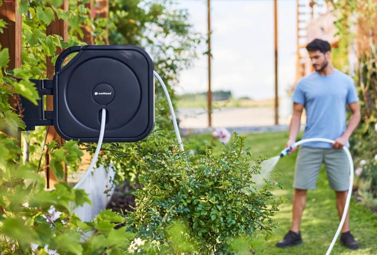 Mężczyzna podlewa ogród za pomocą naściennego zwijacza na wąż