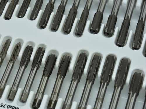 Zestaw narzynek i gwintowników metalowych ułożonych w plastikowej kasecie