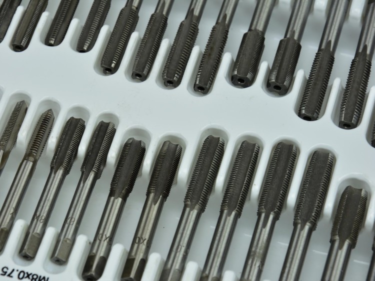 Zestaw narzynek i gwintowników metalowych ułożonych w plastikowej kasecie