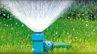 Niebieski zraszacz statyczny WULKAN na szpilce podlewający trawnik z intensywnym strumieniem wody