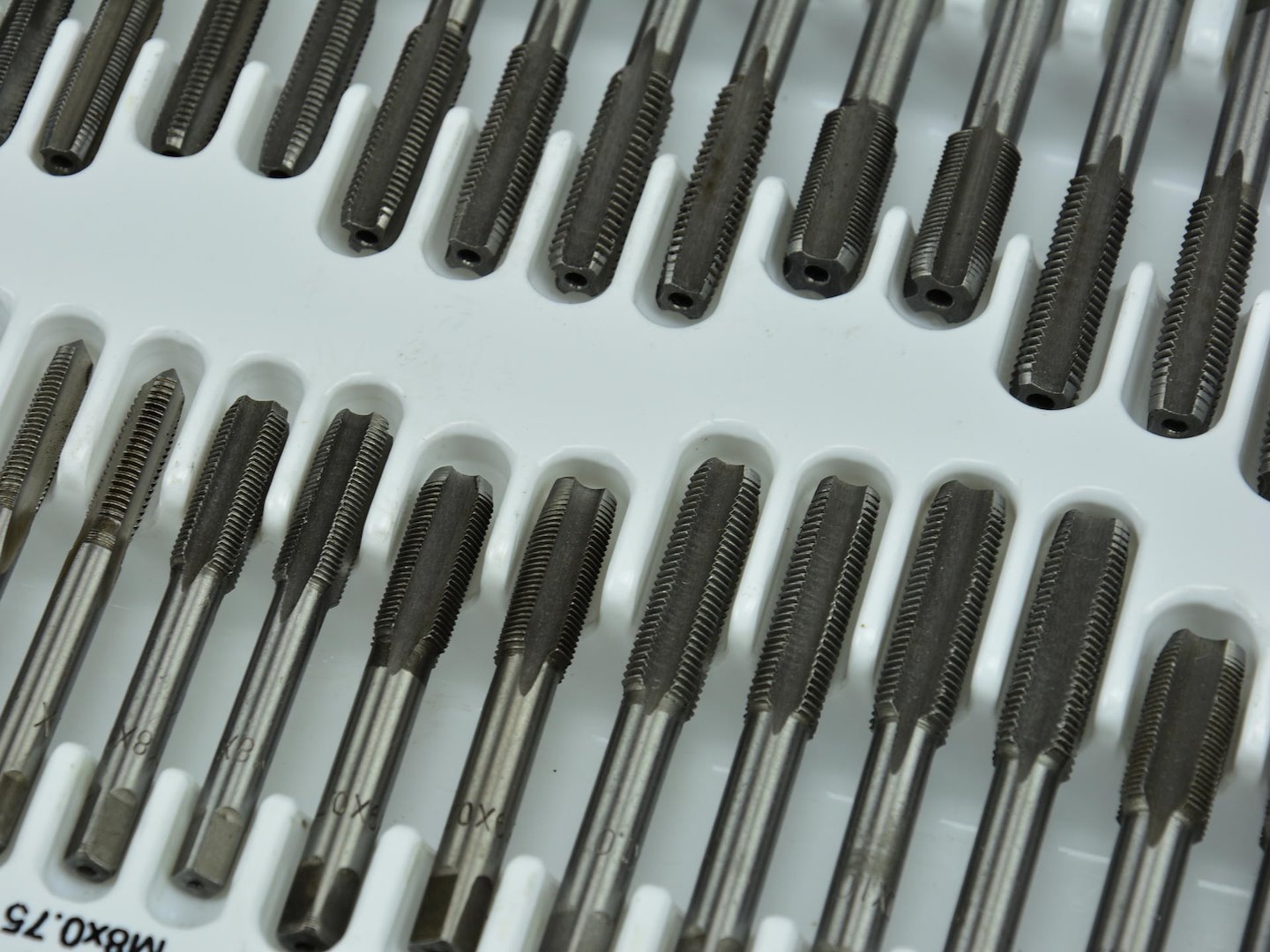 Zestaw narzynek i gwintowników metalowych ułożonych w plastikowej kasecie